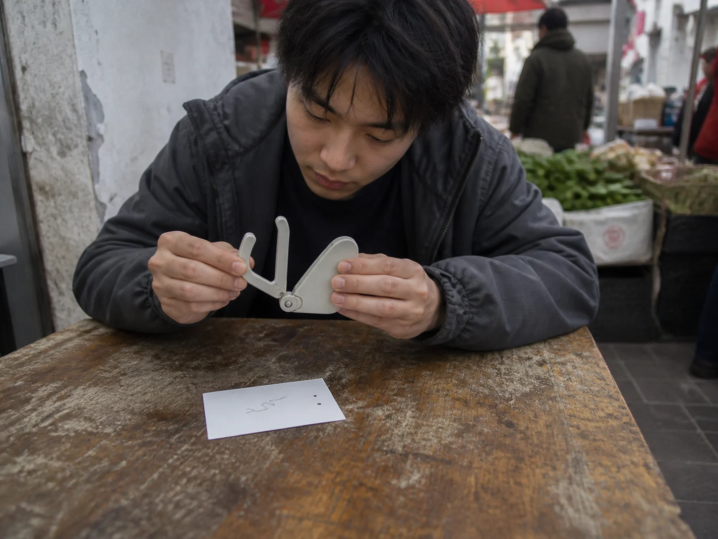 青年在市场边的木桌前检查一个仍待验证的原型部件